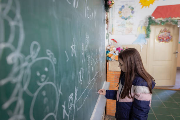 istock Elementary school girl drawing on a chalkboard and decorating a classroom for New Year 1681080049
