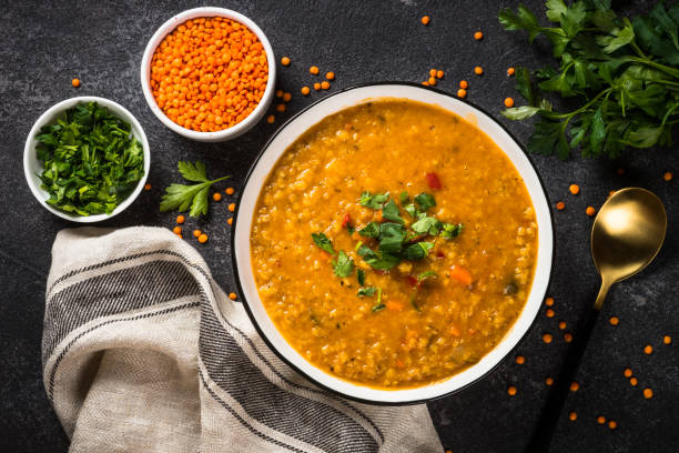 Lentil soup with vegetables on black stone table.
