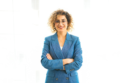 Businesswoman with curly hair in blue jacket with arms crossed in office