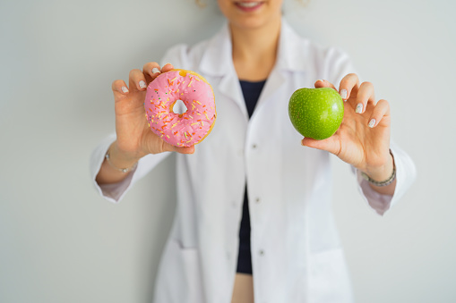 Female healthy nutritionist holding donut and apple with hand. healthy eating life