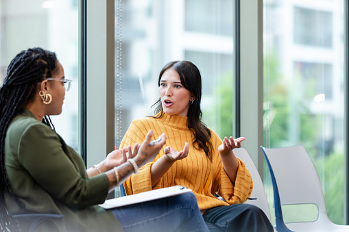 A female therapy patient and female therapist gesture as they discuss something during a therapy session.