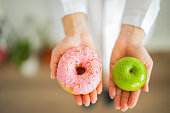 Female healthy nutritionist holding donut and apple with hand. healthy eating life