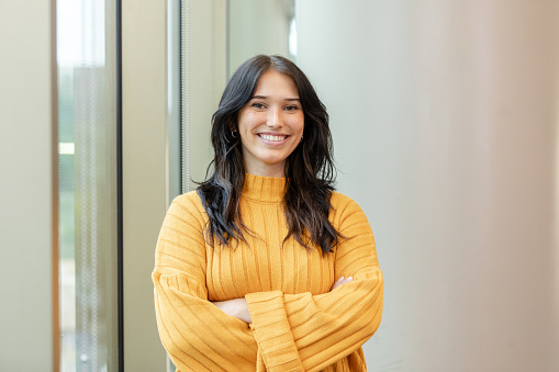 A portrait of a beautiful and confident young adult college student standing with her arms crossed.