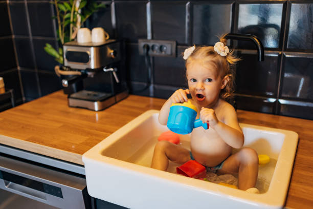istock A cute little girl is looking directly at the camera while taking a bath in the kitchen sink and playing with toys 1681113746