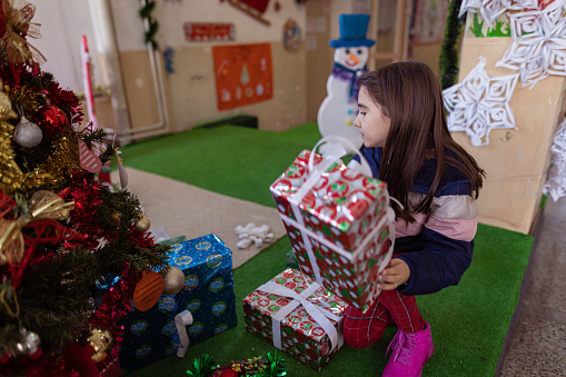 A shot of a little girl playing with a Santa Claus toy in a school lobby, decorated with Christmas ornaments.