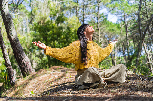 Woman sitting on the woods with arms opened while looking to the sky like thanking God