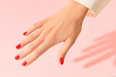 Womans hand with red manicure on pink background. Beauty salon concept