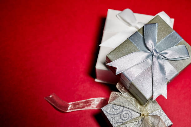Red gift boxes with ribbons and Christmas baubles on white background. Surprises in boxes wrapped in red gift paper with bow. Concept of holidays and greeting cards