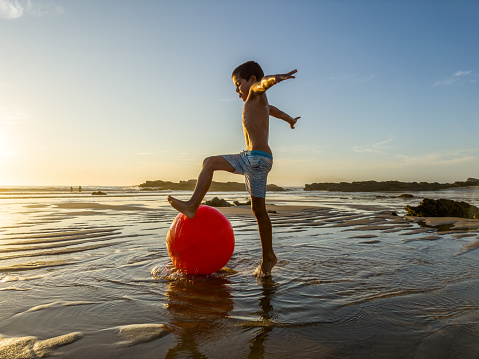 On the empty beach at the end of the day with a ball a child plays