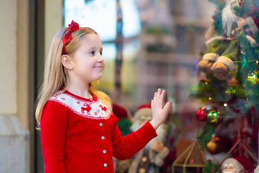 Kids shopping for Christmas presents. Children buy Xmas decoration and tree. Little girl at decorated shop window with lights and Santa toys. Family buying Christmas gifts. Winter holidays.