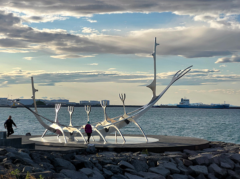 July 16, 2023 - Reykjavik, Iceland.  visitors to the city line up for a photo op in front of the statue.  The Sun Voyager (Sólfarið) is a large steel sculpture of a ship, located on the road Sæbraut, by the seaside of central Reykjavík. The work is one of the most visited sights in the capital, where people gather daily to gaze at the sun reflecting in the stainless steel of this monument.