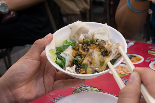 Personal perspective of a mature Chinese man eating local Chinese food with a woman dining companion.  Vegan meal of rice noodles, vegetables and sauce at a busy and crowded night market in Taipei, Taiwan.