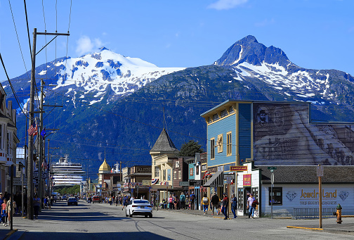 Skagway. Alaska, USA - July 13, 2023:  Twin mountains frame Broadway Street in downtown Skagway. With a cruise ship in the background, cruise passengers shop and enjoy the beauty of Skagway.