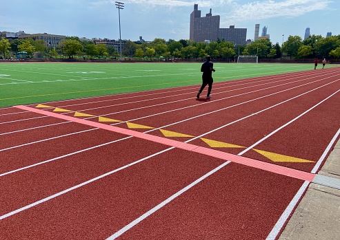 New York, NY USA - September 4, 2023 : African-American man jogging on the red eight-lane outdoor track at Denny Farrell Riverbank State Park on a sunny summer day in West Harlem, New York City, USA