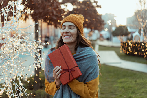 Beautiful woman carrying a Christmas gift and enjoying Christmas Eve in the city