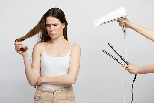 Young woman with beautiful long hair denial to use professional hair straightener and hair dryer, frightened by damaging her silky shiny hair, white background