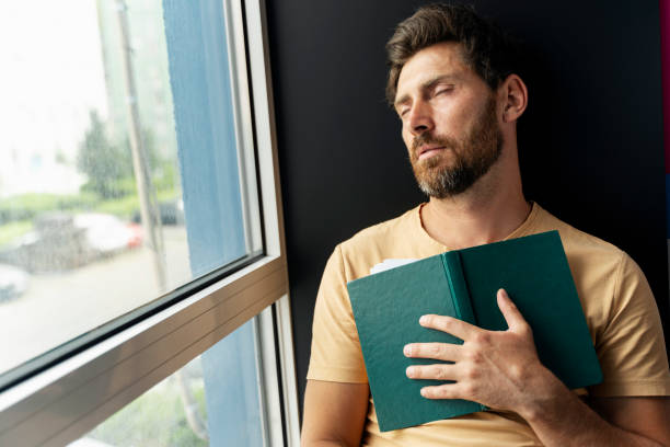 istock Bearded man sleeping, holding book sitting near window. Tired university student in library 1681429786