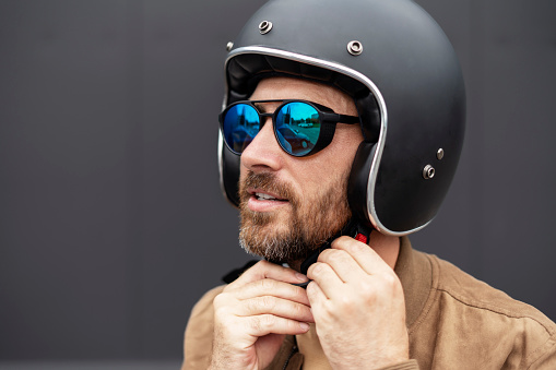 Handsome bearded biker wearing motorcycle helmet and stylish sunglasses ready to ride motorbike. Adventure, freedom, road trip concept