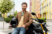 Smiling man biker holding helmet and looking at camera on sport motorcycle