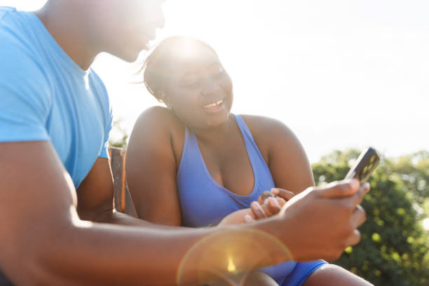 African man and woman holding mobile phone, watching video, text message, social media outdoors