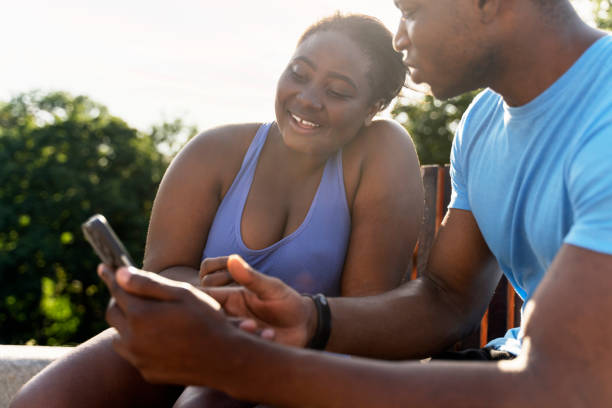 African man and woman holding mobile phone, watching video, text message, social media outdoors