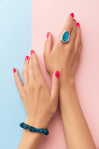 Womans hands with trendy manicure on double pink and blue background. Beauty salon concept. Flat lay, top view, vertical shot