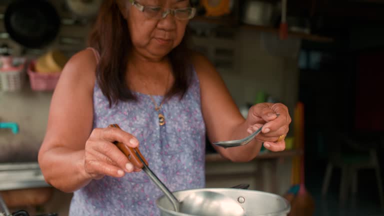 Southeast Asian retired woman cooks food in an imperfect kitchen.