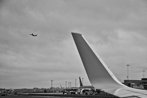 View from the wing of an airplane, watching another airplane in the distance taking off. It is a cloudy and gloomy day.