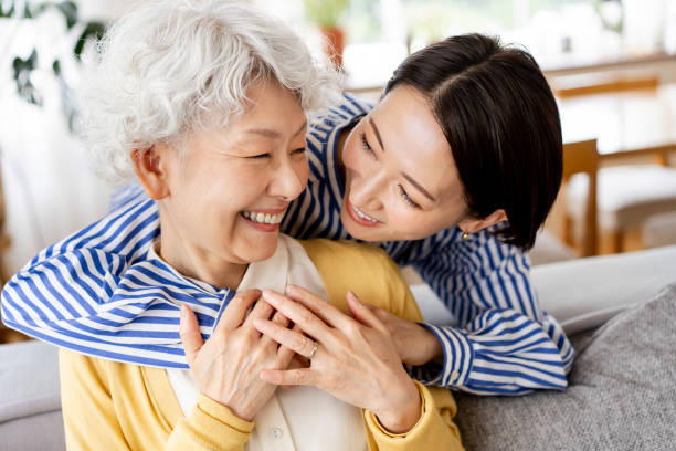 Portrait of two Asian women. Two healthy Japanese women are smiling and hugging each other.They are sitting on the sofa in their living room. mental wellbeing stock pictures, royalty-free photos & images