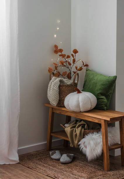 istock Cozy autumn interior of the hallway - an oak bench with a basket with blankets, pillows, branches, pumpkin, slippers on a jute rug 1681760310