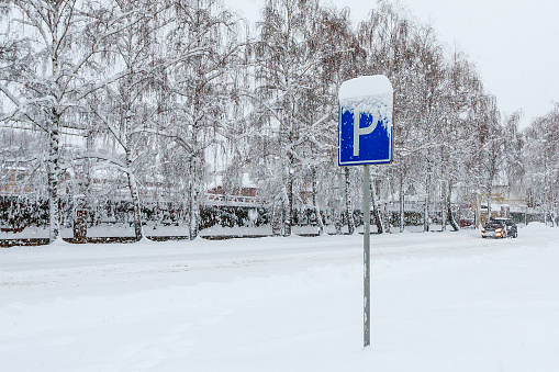 Parking road sign on a snowy street during a snowfall on a winter day. Road sign indicating parking. Parking on the street covered with snow. Abnormal amount of snowfall in winter.