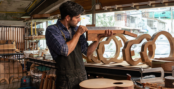 A luthier checks an hollow body guitar neck in his workshop to verify alignment, people arts and craft concept. Work on the creation of the guitar, wood.