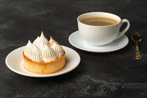 Meringue tart with coffee cup on dark gray background close up