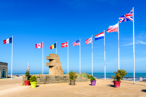 Bernières-sur-Mer, France - Sept. 3, 2023: Signal monument by Yves-Marie Froidevaux erected in 1950 on the WWII Normandy landing site of Juno Beach, surrounded by the national flags of the Allies.