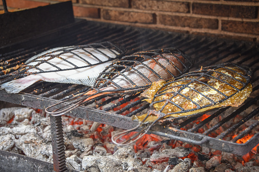 Grilled fish on a bowl-shaped flat grill with fire hole in the center. Outdoor seafood barbecue cooking. Picnic on backyard on open air. Street food concept. Preparing fish over open campfire
