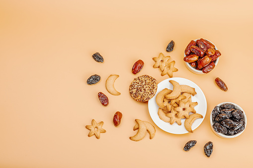 Traditional Ramadan Kareem concept snack for Iftar or Suhoor meal on light orange background. An arabian sweet treat, dates, prunes and cookies. Flat lay, top view