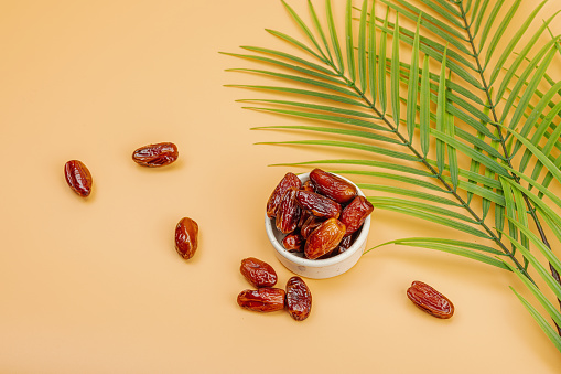Ripe dates, a traditional Ramadan Kareem concept snack for Iftar or Suhoor meal on a light orange background. An Arabian sweet treat, palm leaves, flat lay, top view