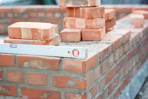Building red brick house wall with spirit level and pile of bricks.