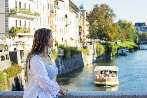 Woman relaxing standing on bridge above Ljubljanica River.