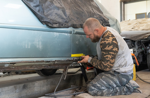 The mechanic removes rust from the surface of a car threshold. The professional auto mechanic repairs the car in his workshop.