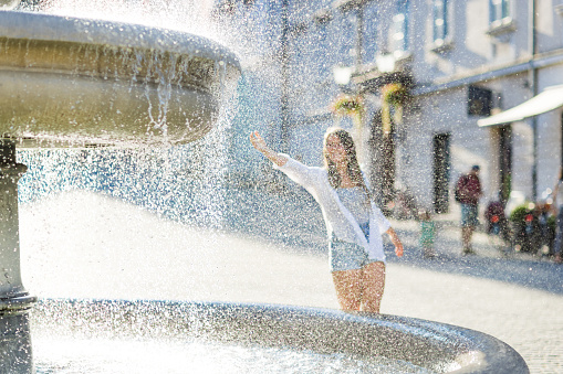 Woman having fun with water next to fountain.