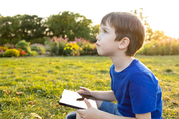 A 6 year old boy uses a digital tablet in a city park
