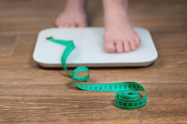 Woman on the scales with a measuring tape, close-up. Diet, healthy lifestyle, weight loss, slim concept. Close-up of the legs of a person standing on the scales stock photo