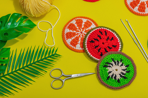 Handmade summer background. Slices of crocheted fruits, traditional accessories, bright yellow color. Balls of threads, hard light, dark shadow, flat lay, top view