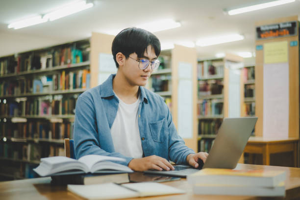 istock Male college students are working on laptops and searching for books to study, make reports, find useful information in college room. Concept of reading, learning and intelligence. 1682011950