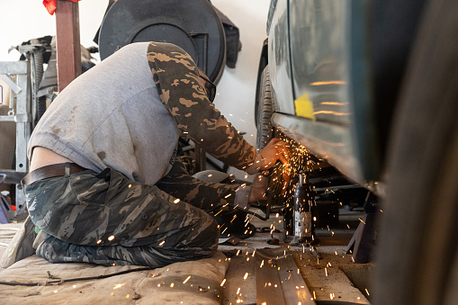 The mechanic uses a grinder to remove rust from the surface of a car's threshold. The professional auto mechanic repairs the car in his workshop.
