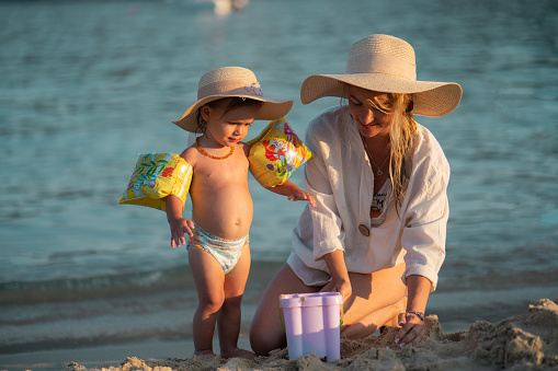 Happy mother and baby girl whit sun hat building sand castle on the beach