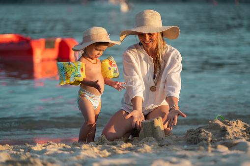 Happy mother and baby girl whit sun hat playing whit sand on the beach
