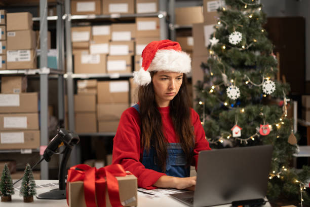 istock Online store inventory manager in Santa hat using laptop, preparing gift parcels for postage. Small business owner working in storeroom at Christmas 1682088178