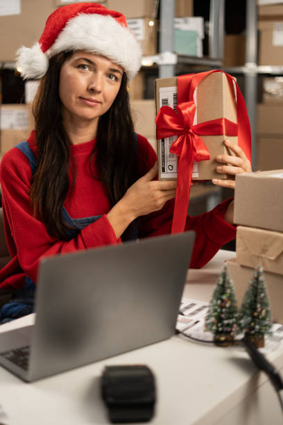 istock Inventory manager preparing a gift parcel for postage. Young female small business owner working on laptop computer in warehouse at Merry Christmas. 1682088688